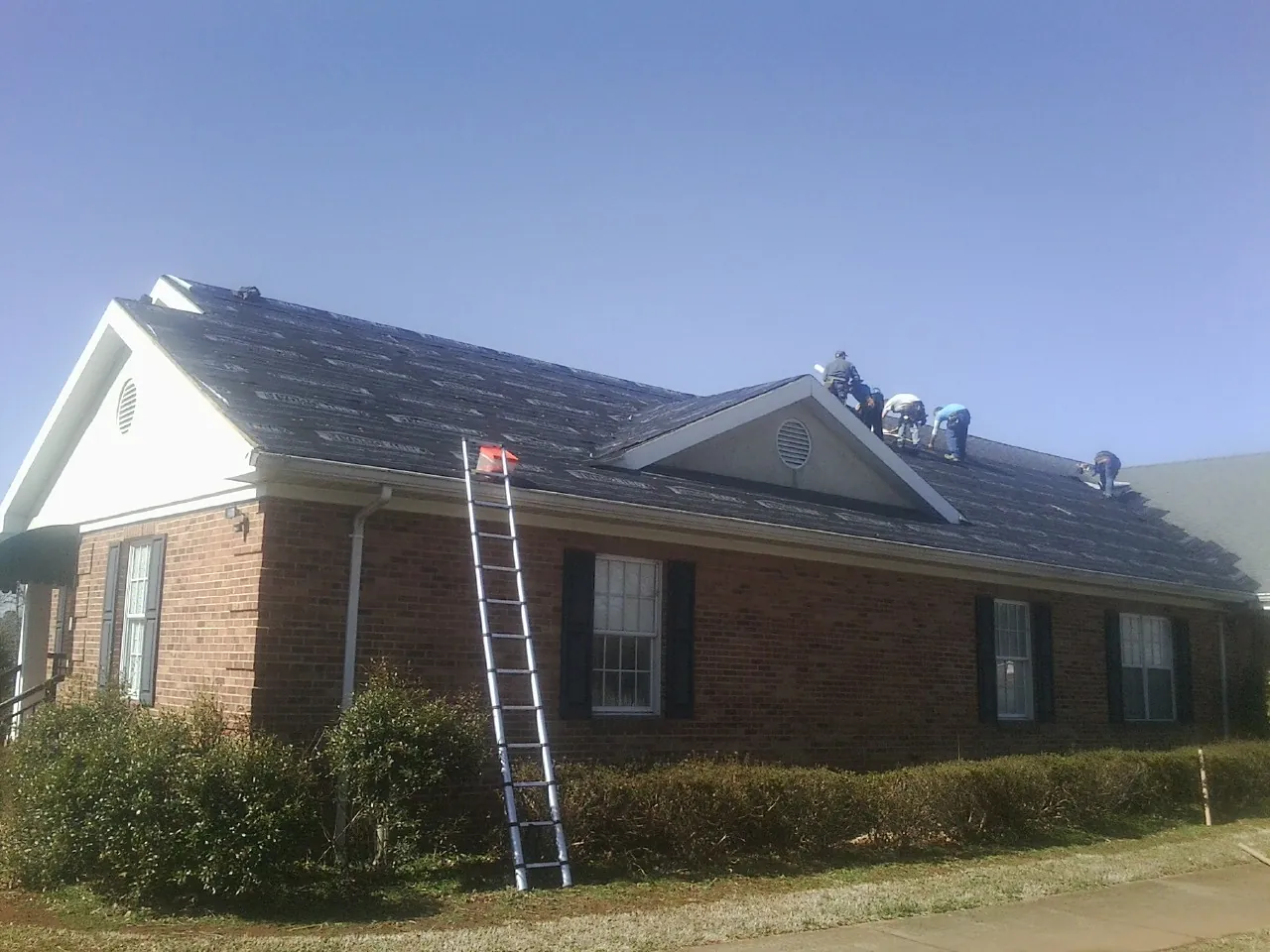 Crew tearing shingles off a brick ranch roof with a ladder set — Metal Roof Repair work by our crew in Commercial Point