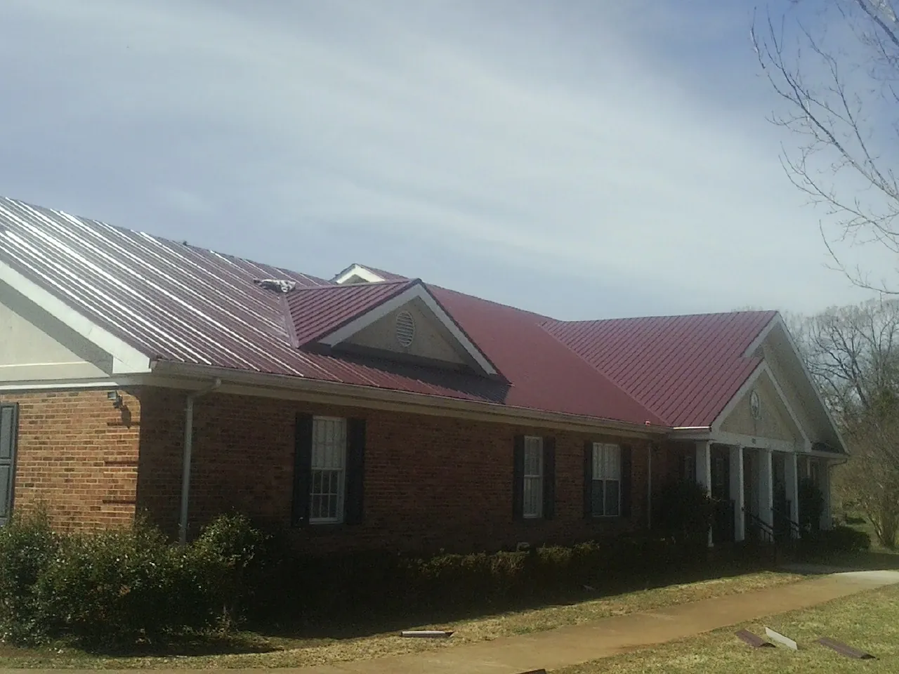 Red metal roof with gabled entries on a long brick building, from a Hail Damage Roof Repair job in Commercial Point