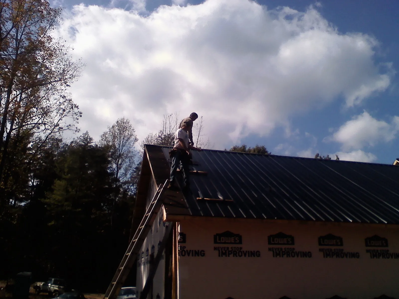 Roofer fastening dark metal panels high against a cloudy sky, from a Roof Inspection job in Commercial Point