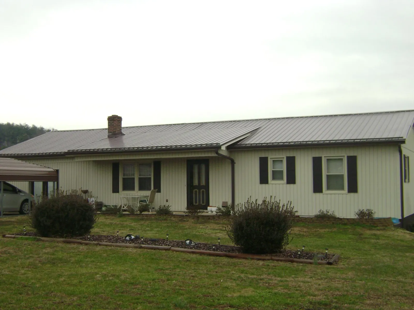 Brown metal roof on a cream sided ranch home with a brick chimney in Commercial Point
