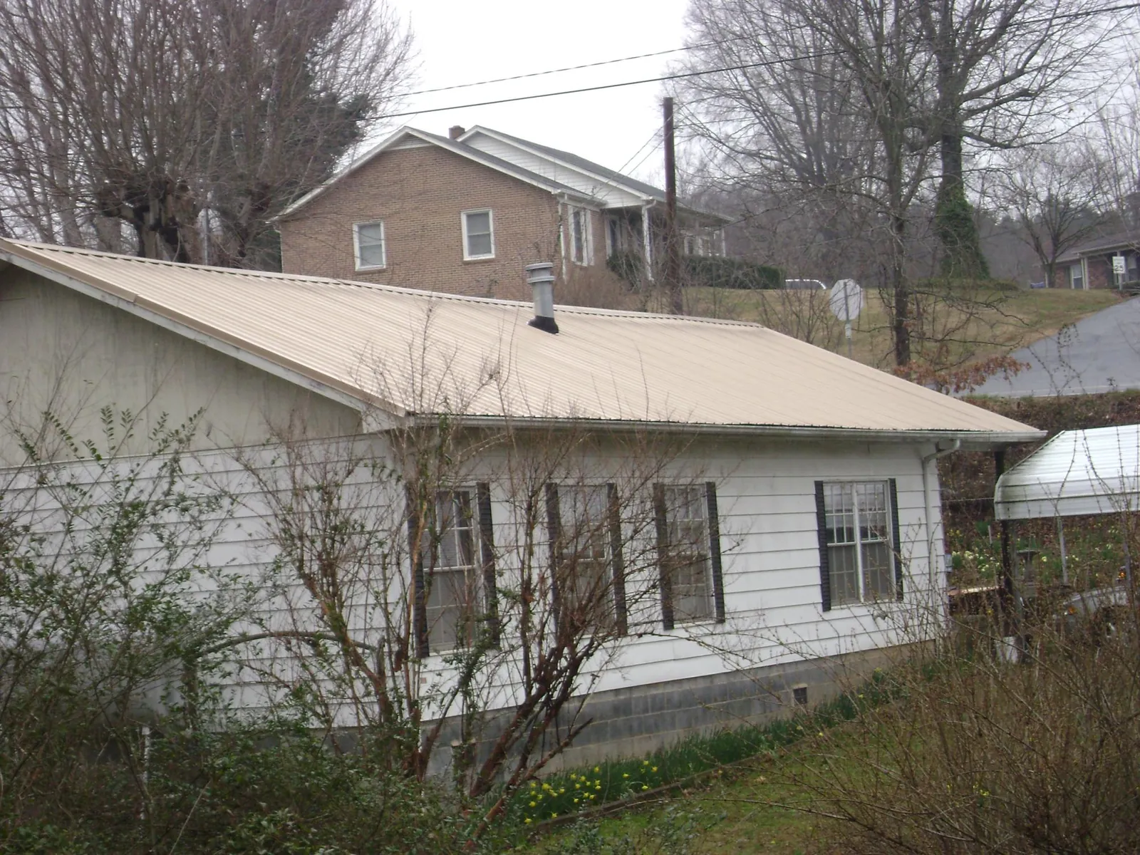 Tan metal roof on a white sided house set into a hillside — Commercial Roofing by Roofing Brothers in Commercial Point