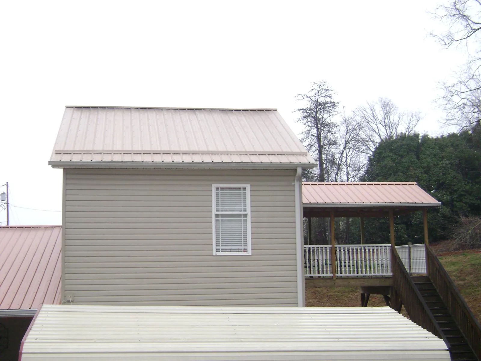 Tan metal roofs on a two story addition and attached porch, from a Roof Replacement job in Commercial Point